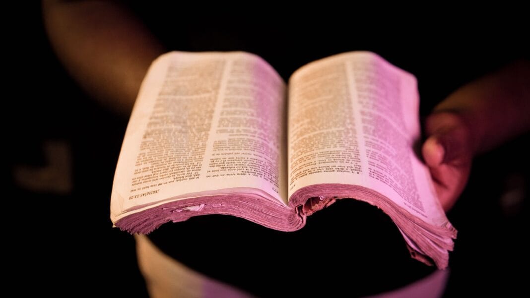 Otwarta Biblia trzymana w dłoniach w dramatycznym świetle
